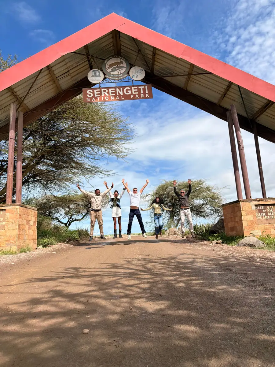 Guests and guides jumping for a photo under the Serengeti National Park entrance sign
