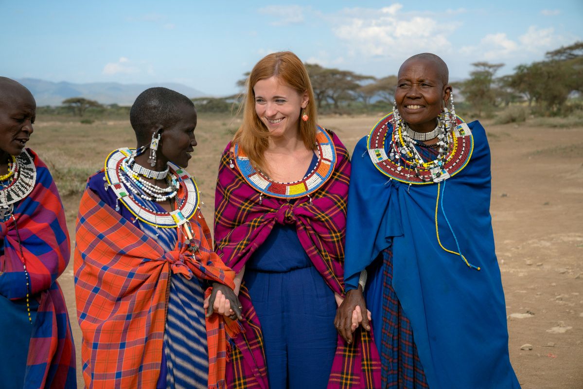 A traveller holding hands with Maasai women wearing traditional shukas