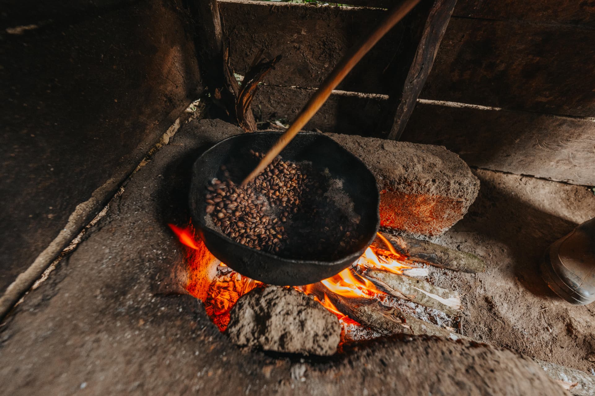 Fresh coffee beans being roasted in a black pan over glowing coals