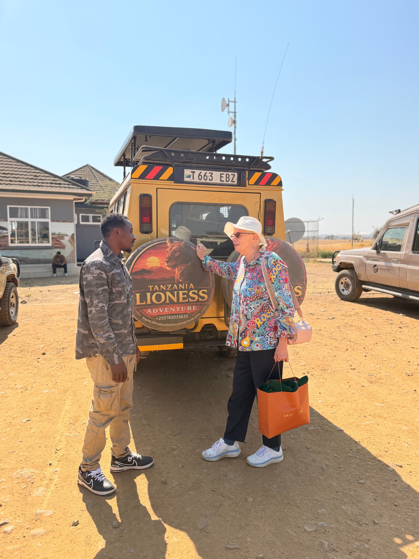 A Tanzania Lioness Adventure guide talking with a guest beside the safari vehicle