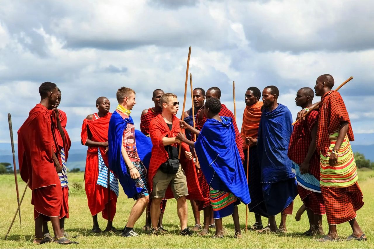Travellers wrapped in shukas joining Maasai men on the grassland