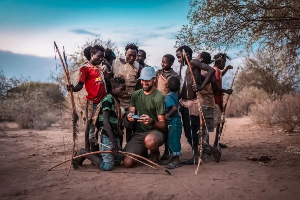 A traveller sitting with Hadzabe men holding traditional bows