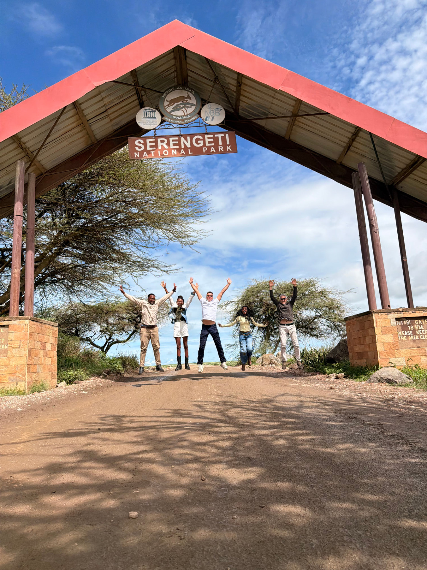 Guests and guides jumping for a photo under the Serengeti National Park entrance sign